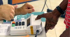 #PraTodosVerem: Na fotografia uma mão fazendo a identificação biométrica na mesa de votação da s...